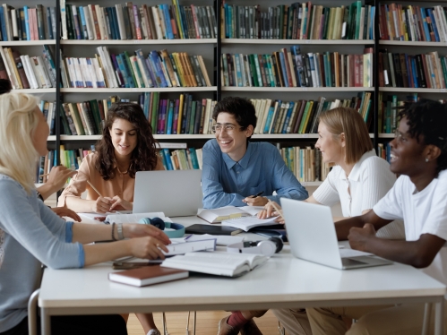 Stock photograph of 5 people sitting around table with paper and laptops working together